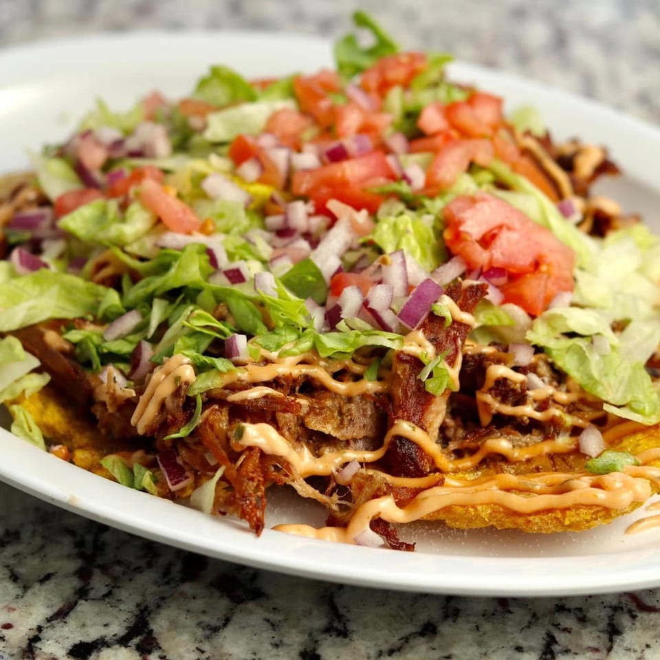 Loaded fries topped with shredded lettuce, diced tomatoes, red onions, crispy meat, and creamy orange sauce on a white plate.