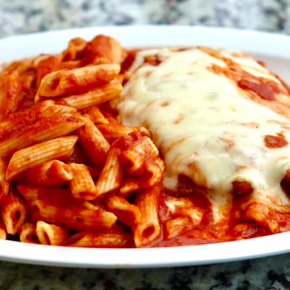 Plate of penne pasta in tomato sauce alongside breaded chicken topped with melted cheese and marinara sauce.